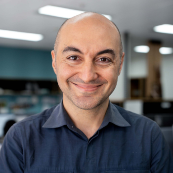 A smiling man in a navy shirt standing in a brightly lit office environment.